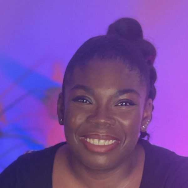 Carlene smiling, hair up in a bun, in purple studio light
