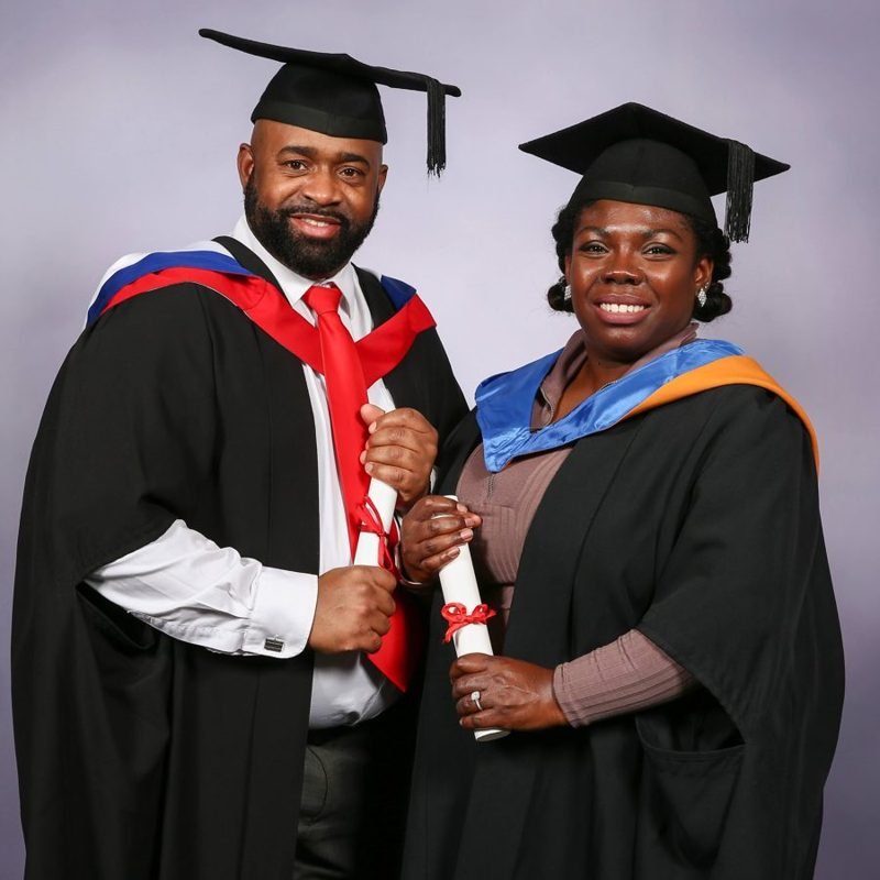 Bear and Carlene in graduation gowns and caps, each holding a rolled certificate